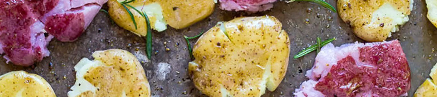 Smashed potatoes with rosemary on a tray.